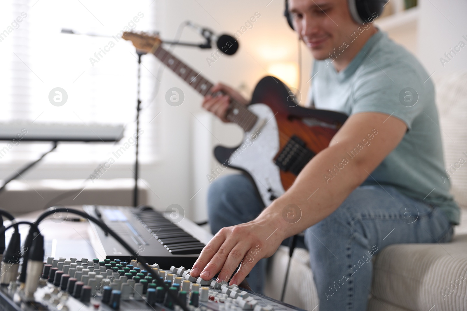 Photo of Man working with guitar, dj mixer and MIDI keyboard on sofa in home studio, selective focus