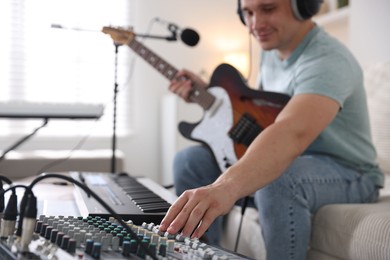 Photo of Man working with guitar, dj mixer and MIDI keyboard on sofa in home studio, selective focus