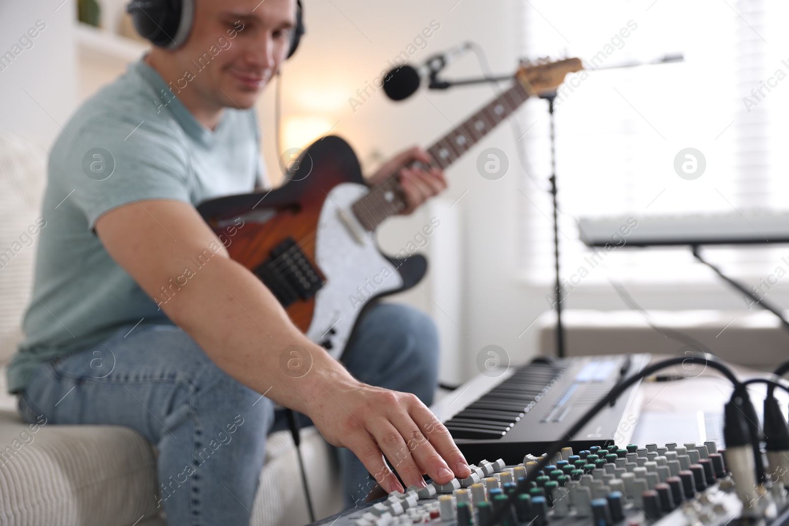 Photo of Man working with guitar, dj mixer and MIDI keyboard on sofa in home studio, selective focus
