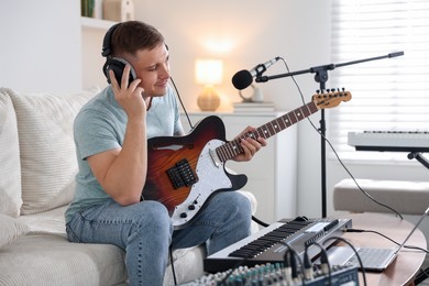 Photo of Man in headphones working with guitar and MIDI keyboard on sofa in home studio
