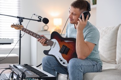 Photo of Man in headphones working with guitar and MIDI keyboard on sofa in home studio