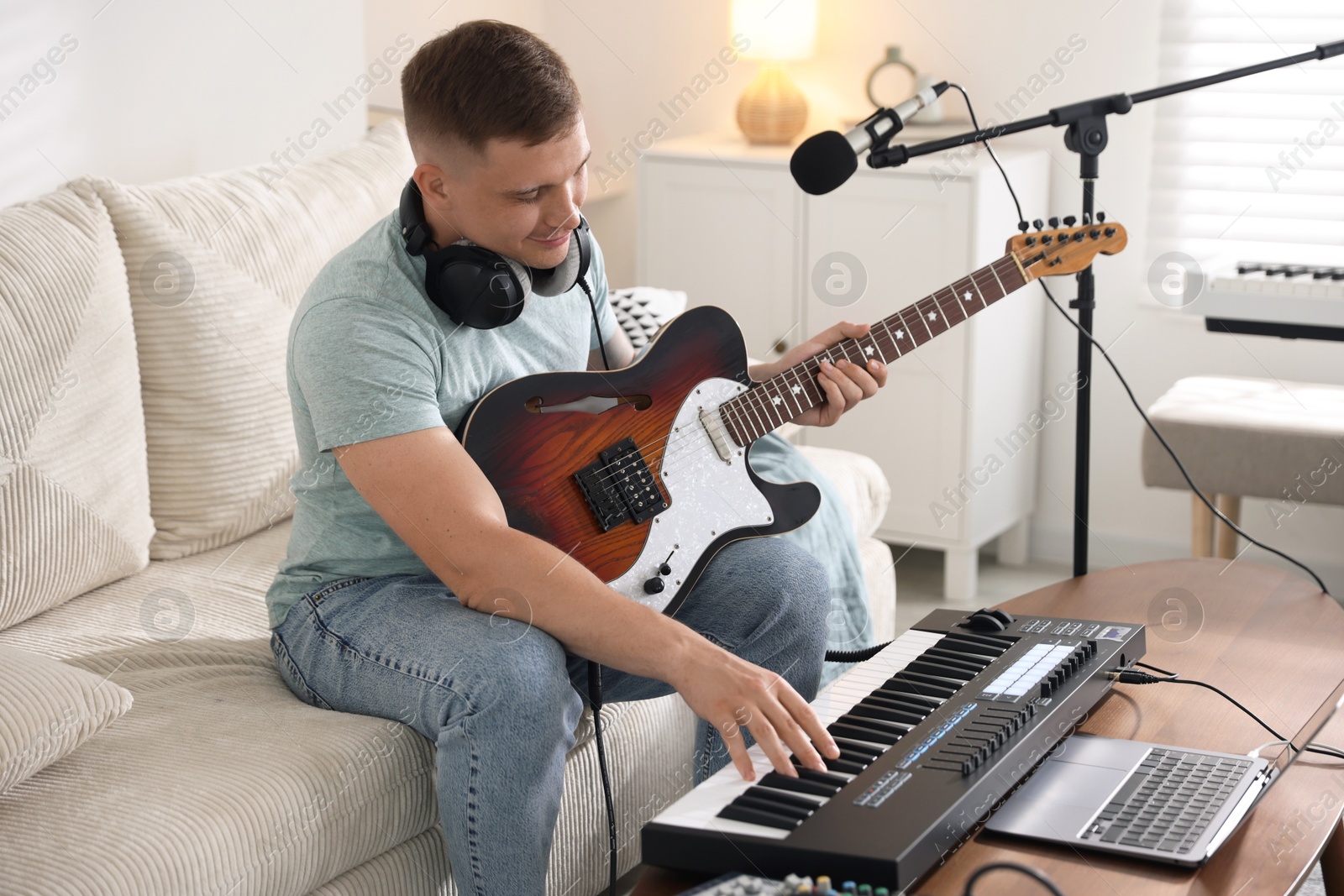 Photo of Man working with guitar and MIDI keyboard on sofa in home studio