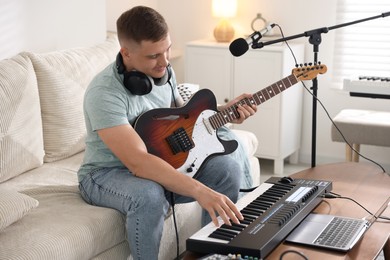 Photo of Man working with guitar and MIDI keyboard on sofa in home studio