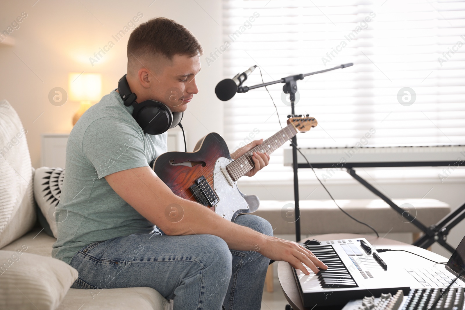 Photo of Man working with guitar and MIDI keyboard on sofa in home studio