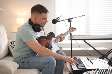 Photo of Man working with guitar and MIDI keyboard on sofa in home studio