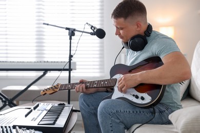 Photo of Man working with guitar and MIDI keyboard on sofa in home studio