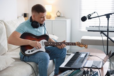 Photo of Man working with guitar and MIDI keyboard on sofa in home studio