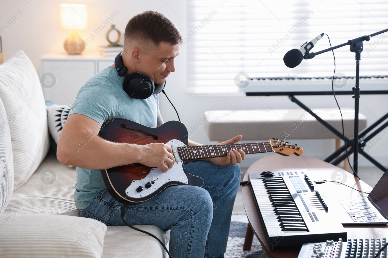 Photo of Man working with guitar and MIDI keyboard on sofa in home studio