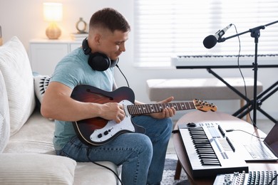 Photo of Man working with guitar and MIDI keyboard on sofa in home studio