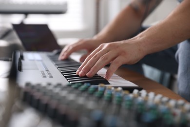 Photo of Man working with MIDI keyboard at table indoors, closeup