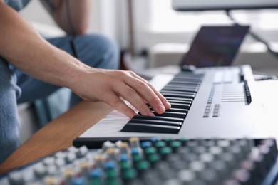 Photo of Man working with MIDI keyboard at table indoors, closeup
