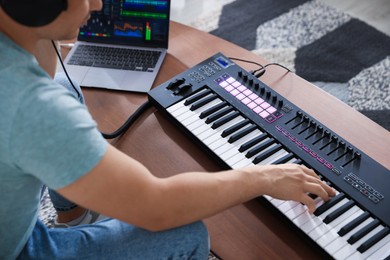 Photo of Man working with MIDI keyboard and laptop at table indoors, closeup