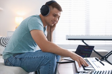 Photo of Man in headphones working with MIDI keyboard at table indoors