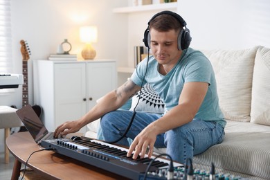 Photo of Man in headphones working with MIDI keyboard and laptop at table indoors