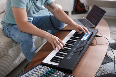 Photo of Man working with MIDI keyboard at table indoors, closeup