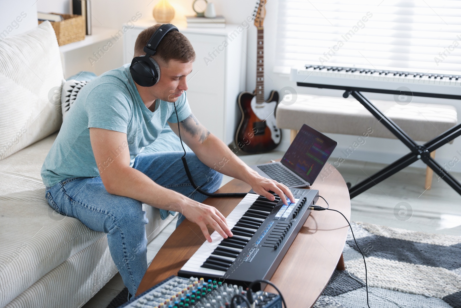 Man in headphones working with MIDI keyboard at table indoors Photo of Man in headphones working with MIDI keyboard at table indoors
