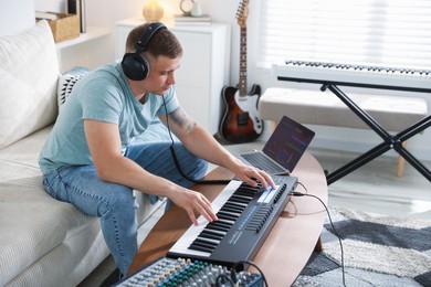 Photo of Man in headphones working with MIDI keyboard at table indoors
