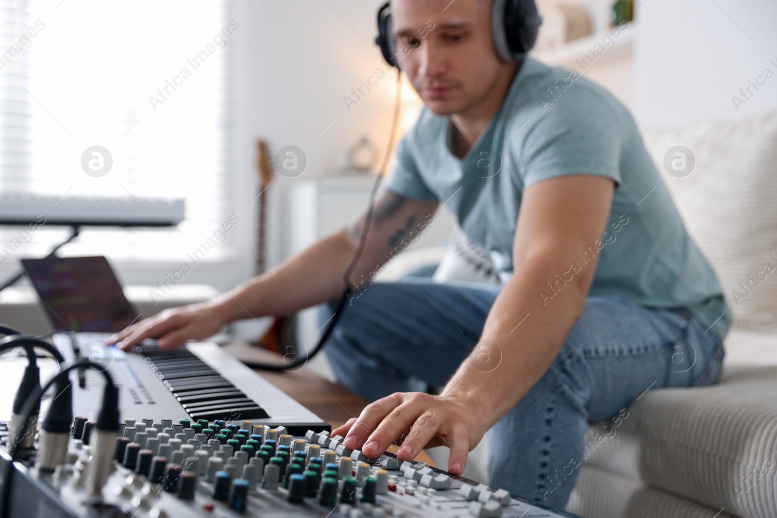 Photo of Man working with dj mixer and MIDI keyboard on sofa indoors, selective focus