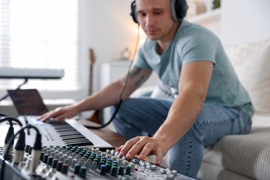 Photo of Man working with dj mixer and MIDI keyboard on sofa indoors, selective focus