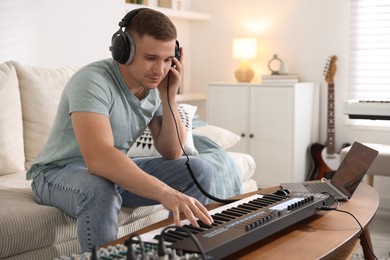 Photo of Man in headphones working with MIDI keyboard at table indoors