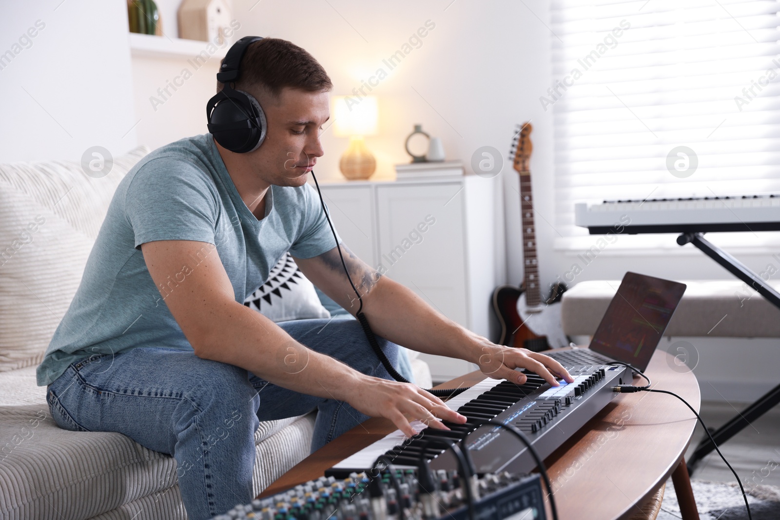 Man in headphones working with MIDI keyboard at table indoors Photo of Man in headphones working with MIDI keyboard at table indoors