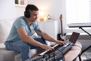 Photo of Man in headphones working with MIDI keyboard at table indoors