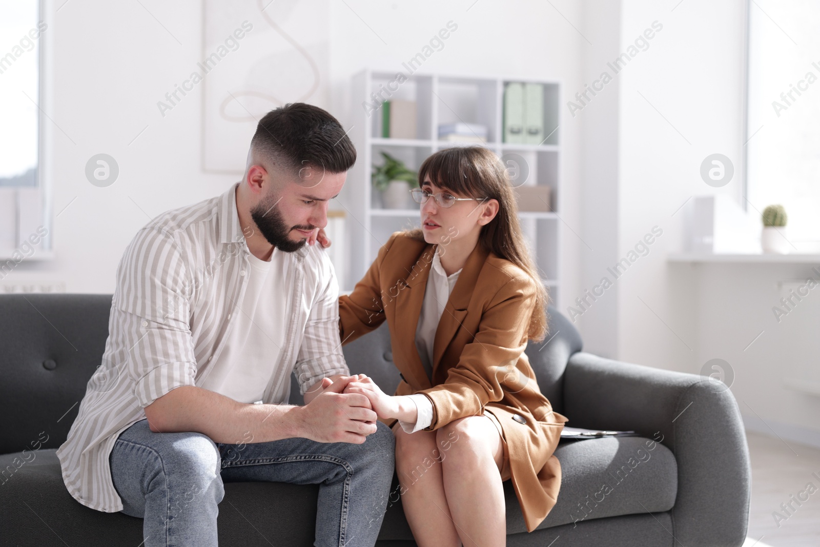 Photo of Psychologist supporting patient during therapy session on sofa in office