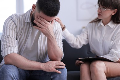 Photo of Psychologist supporting patient during therapy session on sofa in office