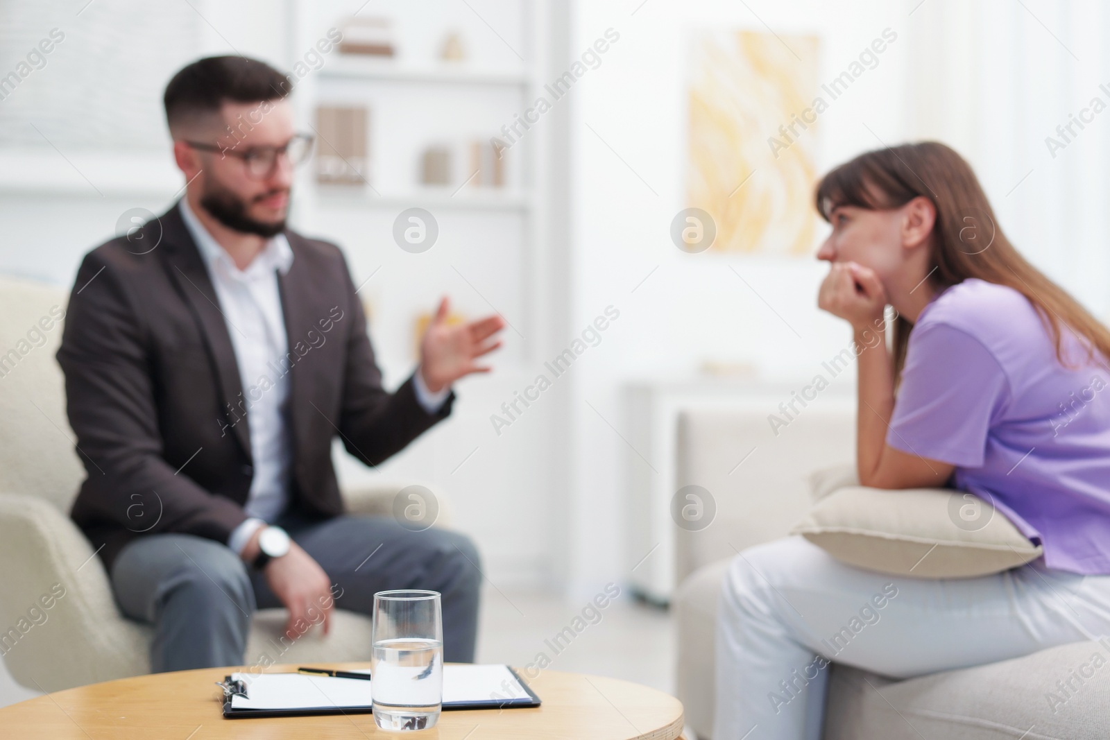 Photo of Professional psychologist working with patient in office, focus on glass of water