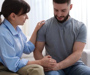 Photo of Psychologist supporting patient during therapy session on sofa in office