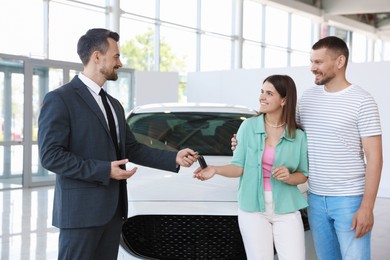 Photo of Smiling salesman giving car key to happy family in salon