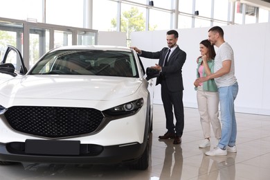 Photo of Salesman showing new car to happy family in salon