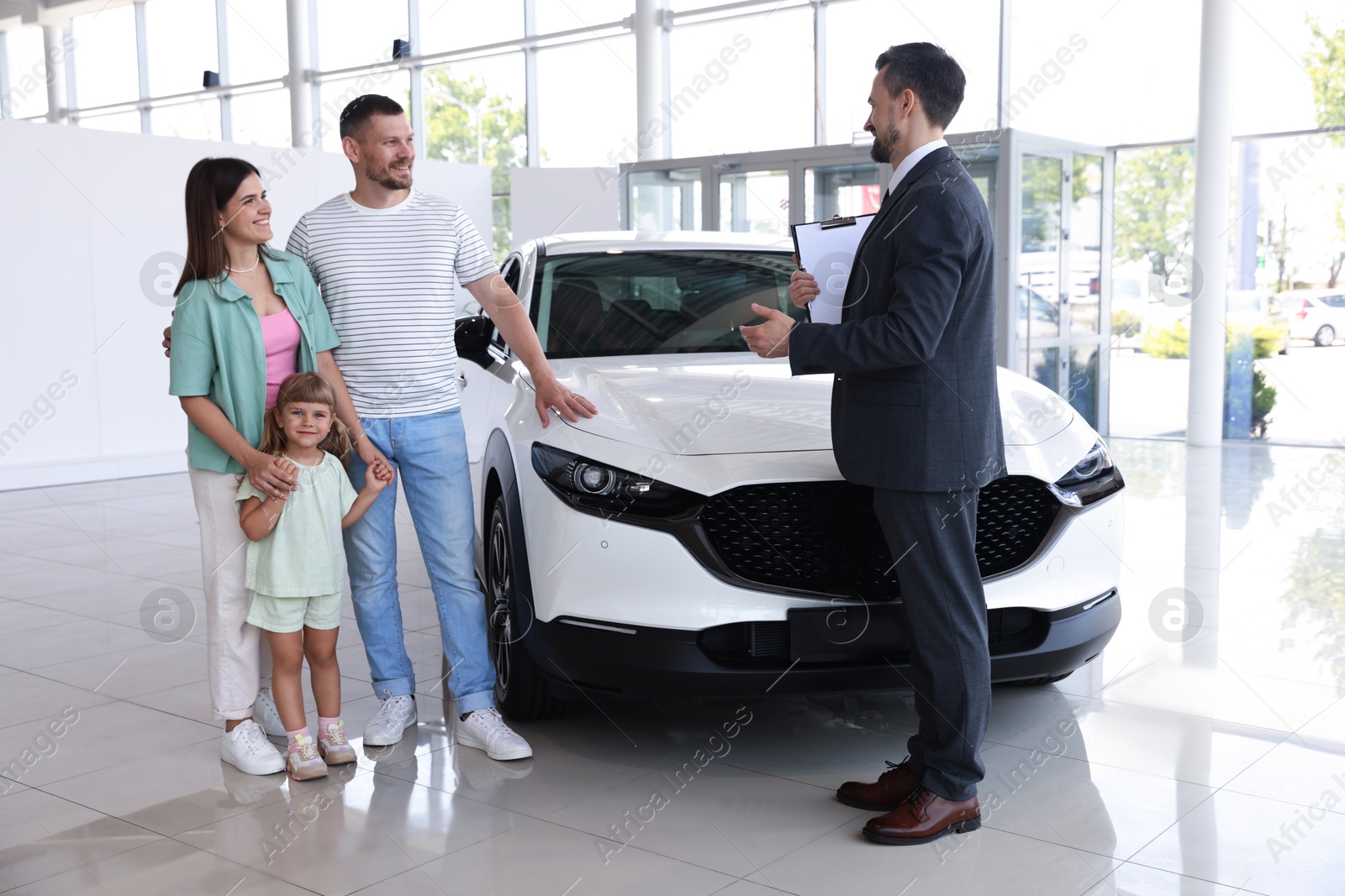 Photo of Salesman with clipboard showing new car to happy family in salon