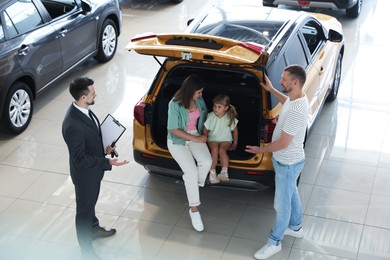 Photo of Salesman with clipboard showing new car to family in salon