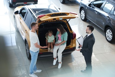 Photo of Salesman with clipboard showing new car to family in salon