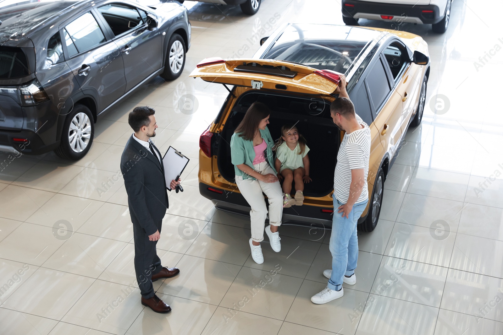 Photo of Salesman with clipboard showing new car to family in salon