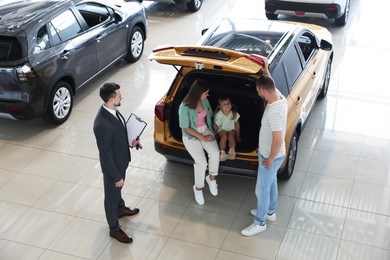 Photo of Salesman with clipboard showing new car to family in salon