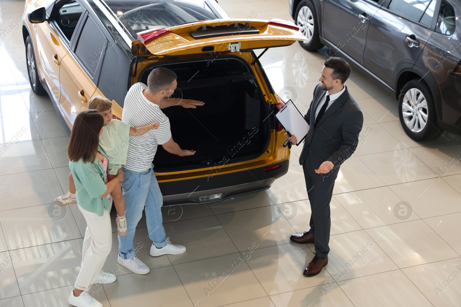 Photo of Salesman with clipboard showing new car to family in salon
