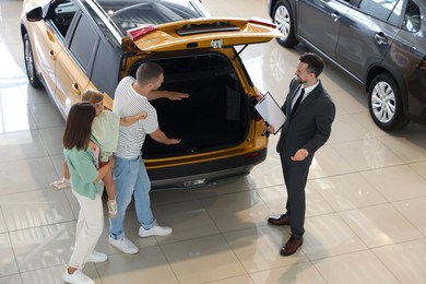 Photo of Salesman with clipboard showing new car to family in salon