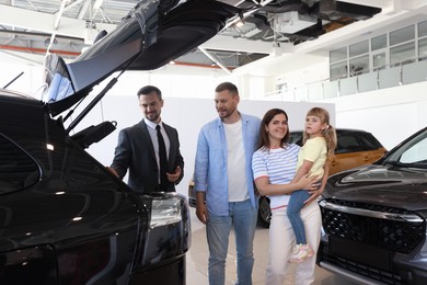 Photo of Salesman showing new car to happy family in salon