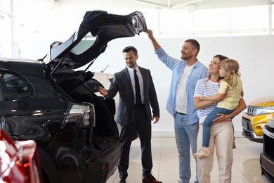 Photo of Salesman showing new car to happy family in salon