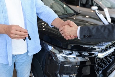 Photo of Salesman shaking hands with man near new car in salon, closeup