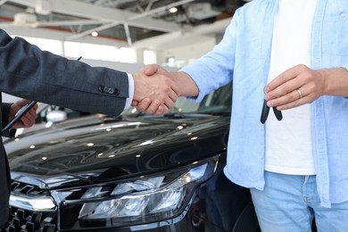 Photo of Salesman shaking hands with man near new car in salon, closeup