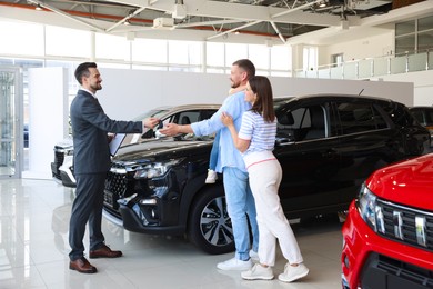 Photo of Salesman giving car key to happy family in salon