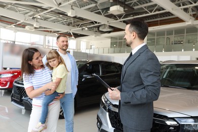 Photo of Salesman with clipboard working with happy family in car salon