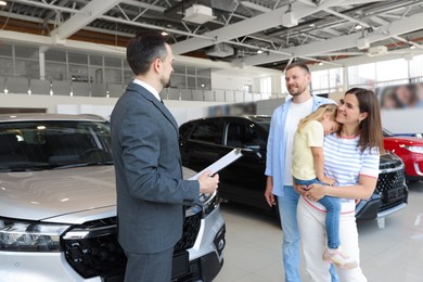 Photo of Salesman with clipboard working with happy family in car salon