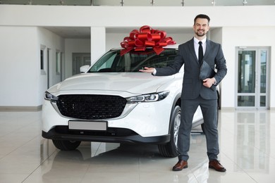 Photo of Smiling salesman with clipboard showing new car in salon