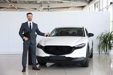 Photo of Smiling salesman with clipboard showing new car in salon