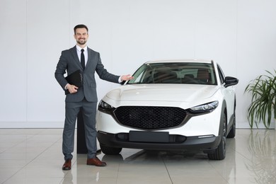 Photo of Smiling salesman with clipboard showing new car in salon