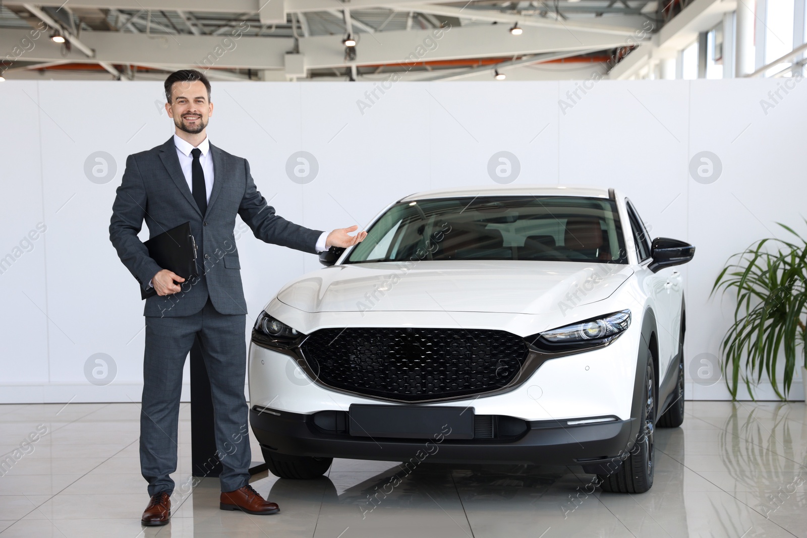 Photo of Smiling salesman with clipboard showing new car in salon